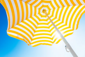 Kelta-valkoraidallinen aurinkovarjo sinistä taivasta vasten.