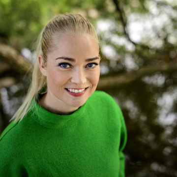 Vaaleatukkainen nainen vihreässä puserossa hymyilee kameralle.