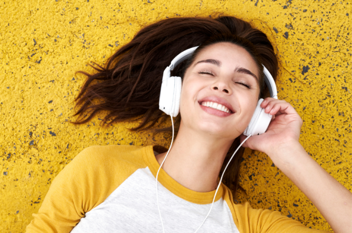 Nainen makaa keltaisen alustan päällä ja kuuntelee kuulokkeilla musiikkia.