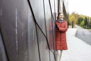 Mikaela Kulo seisoo kirjaston seinän vieressä punainen takki päällään.