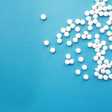Valkoisia lääketabletteja hajallaan sinisellä tasolla.