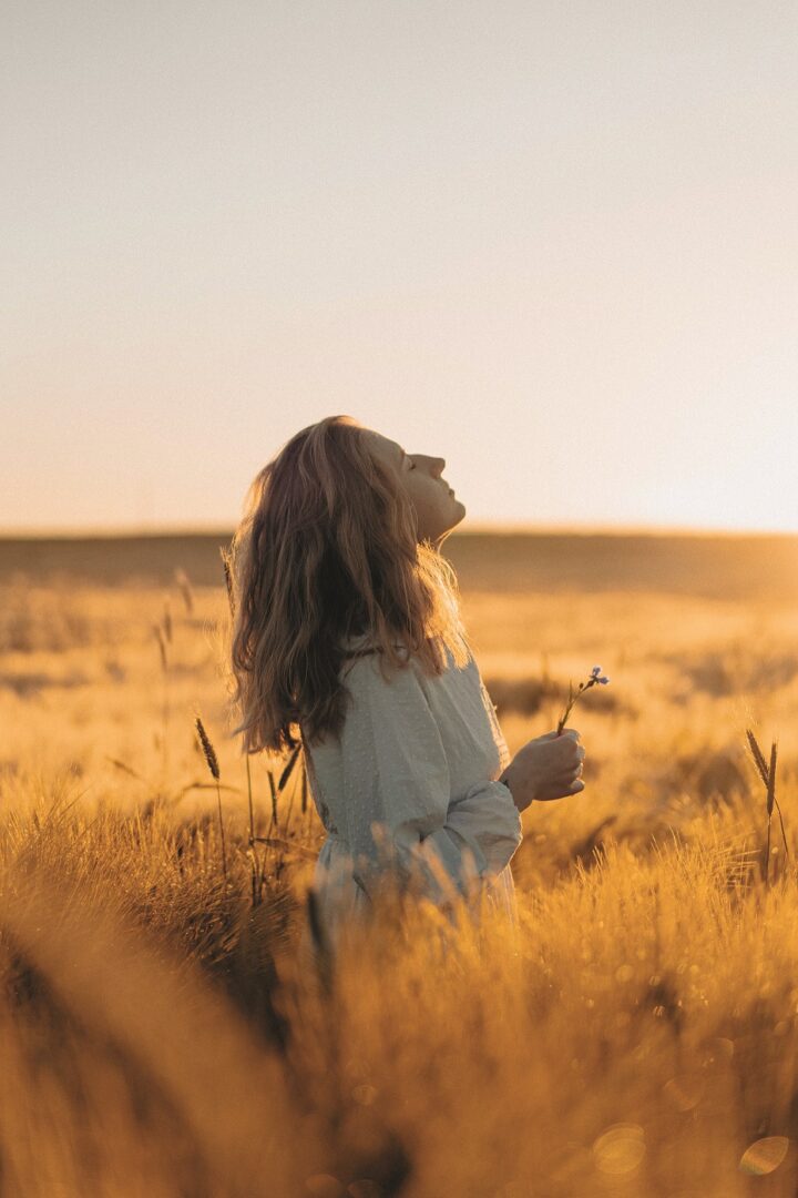 Nainen seisoo pellolla silmät kiinni kasvot kohti aurinkoa.