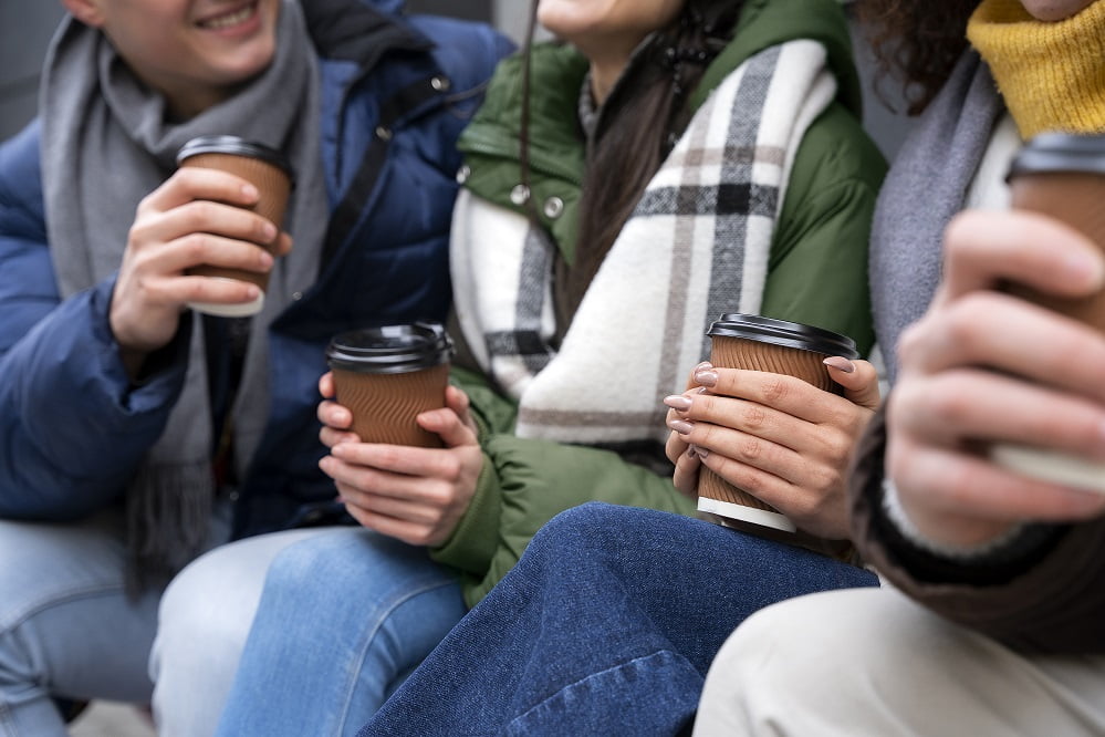 Ihmisiä istuu ulkona kahvikupit kädessään.