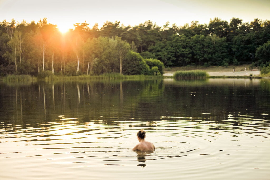 Ihminen ui järvessä ilta-auringossa.