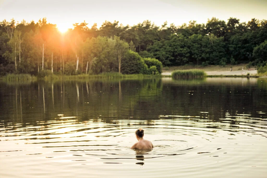 Ihminen ui järvessä ilta-auringossa.