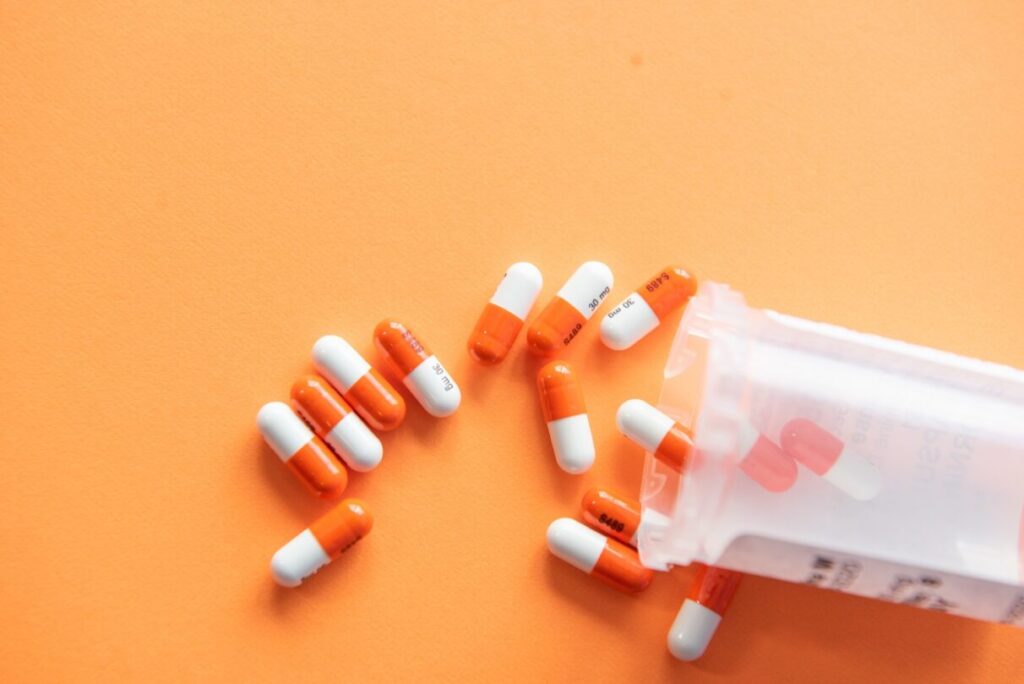 Oranssi-valkoisia lääkepillereitä oranssilla taustalla.
