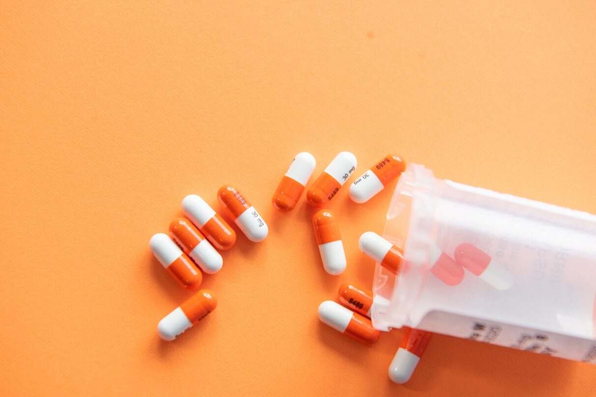 Oranssi-valkoisia lääkepillereitä oranssilla taustalla.