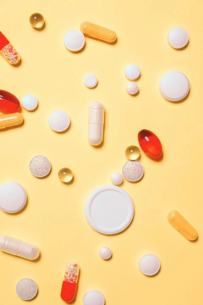 Erilaisia lääketabletteja vaaleankeltaisella tasolla.
