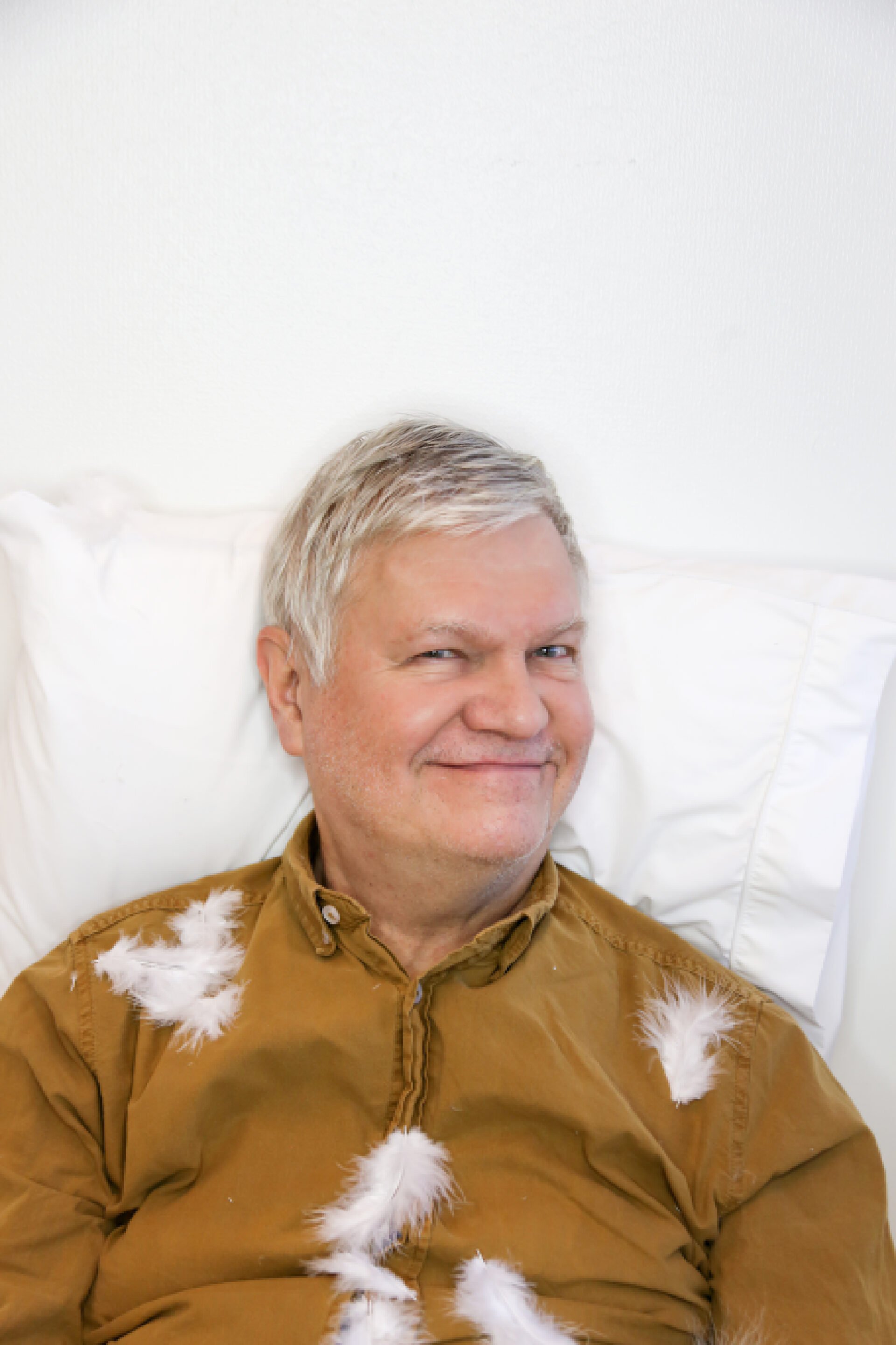 Markku Partinen makaa tyynyllä ja hänen päällään leijailee höyheniä.