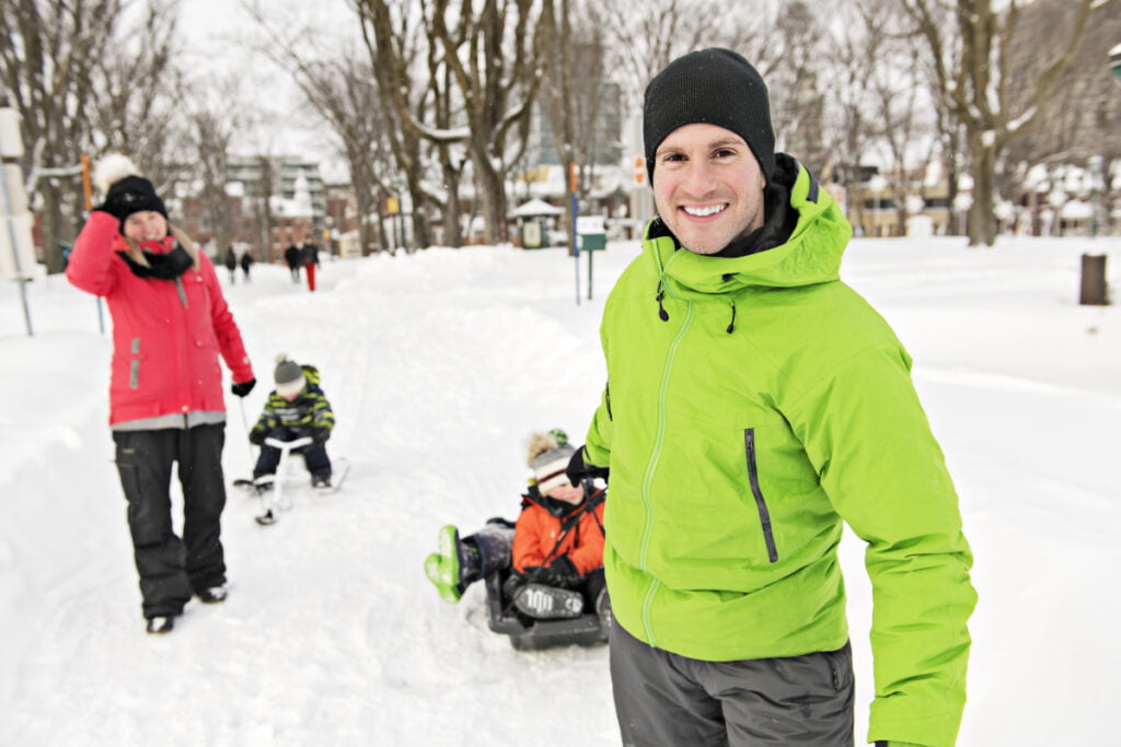 Nainen ja mies vetävät lapsia pulkassa lumisessa maisemassa.