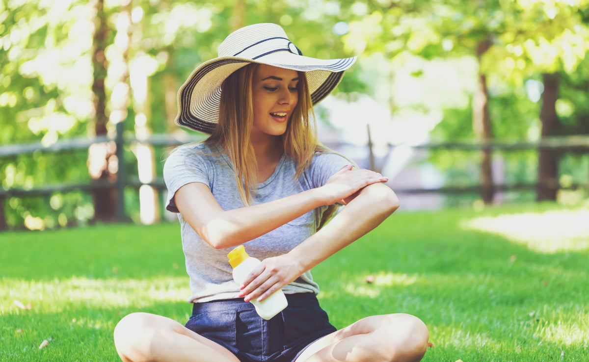 Nainen istuu nurmikolla ja levittää aurinkovoidetta käsivarteen.