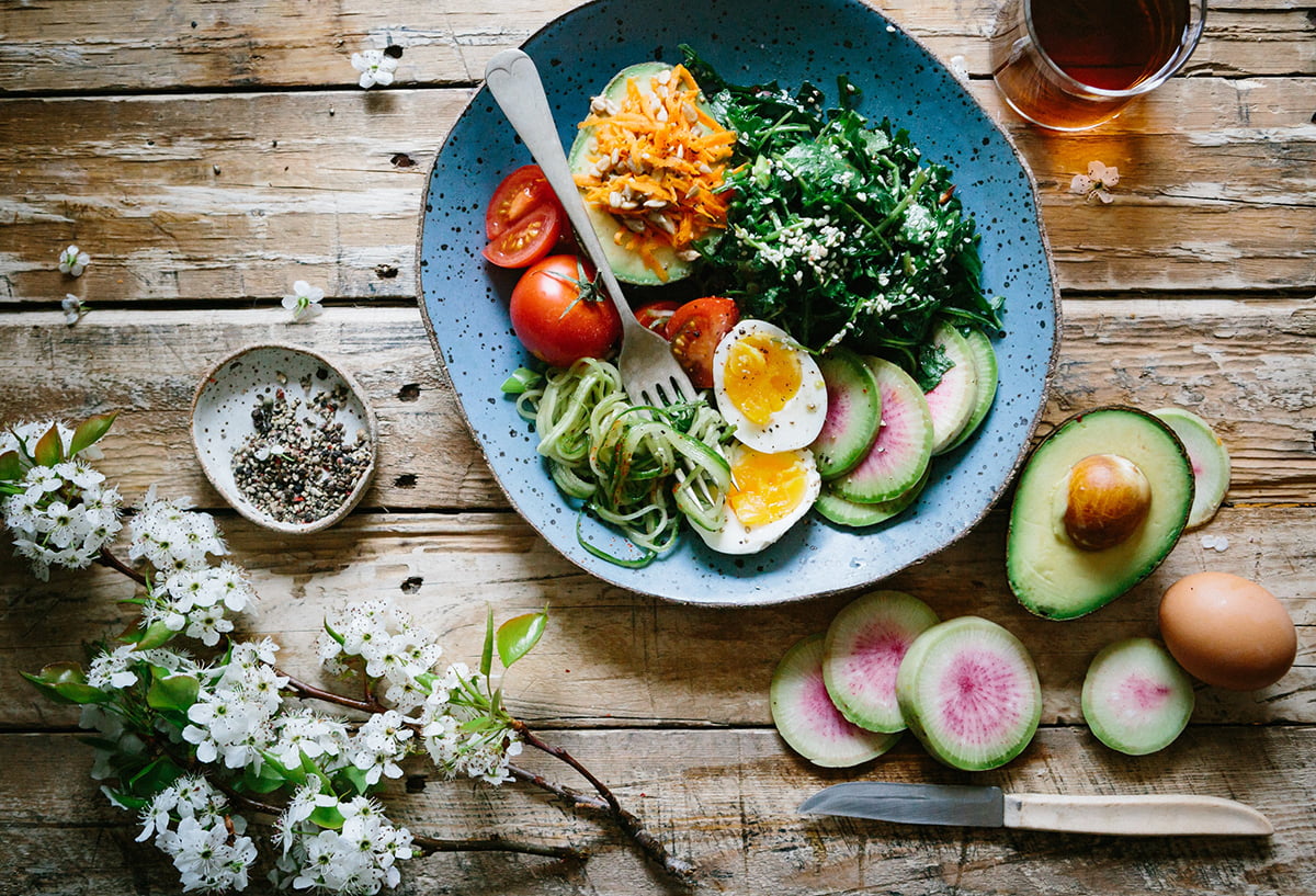 Pöydällä on lautanen, jossa on terveellistä ruokaa, kuten kasviksiä, siemeniä ja keitetty kananmuna.