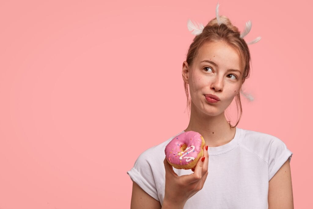 Nainen pitelee kädessään vaaleanpunaista donitsia.